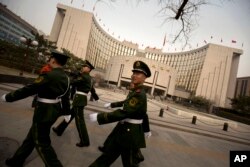 FILE - Chinese paramilitary police march past China's central bank, the People's Bank of China, in Beijing.