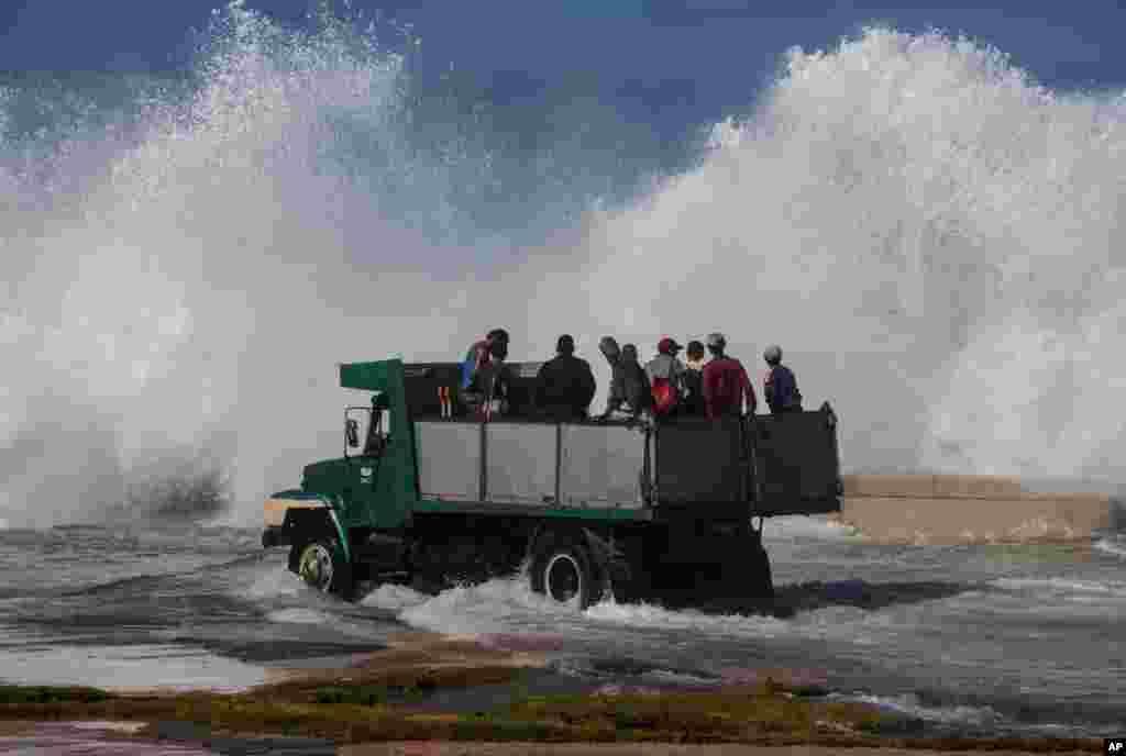A dump truck carrying cleaning workers drives on Havana's Malecón as a wave crashes on the sea wall, in Cuba.