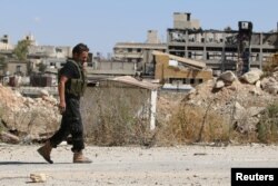 A rebel fighter walks by damaged buildings near Castello road in Aleppo, Syria, Sept. 16, 2016.