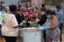 FILE - Children line up for food at a feeding scheme in Lavender Hill, Cape Town, South Africa, April 21, 2020, during the fourth week of lockdown to contain the spread of coronavirus.