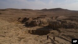 FILE - Two Iraqi men walk near a sinkhole known as Khasfa, that is believed to contain the remains of people executed by Islamic State militants south of Mosul, Iraq.