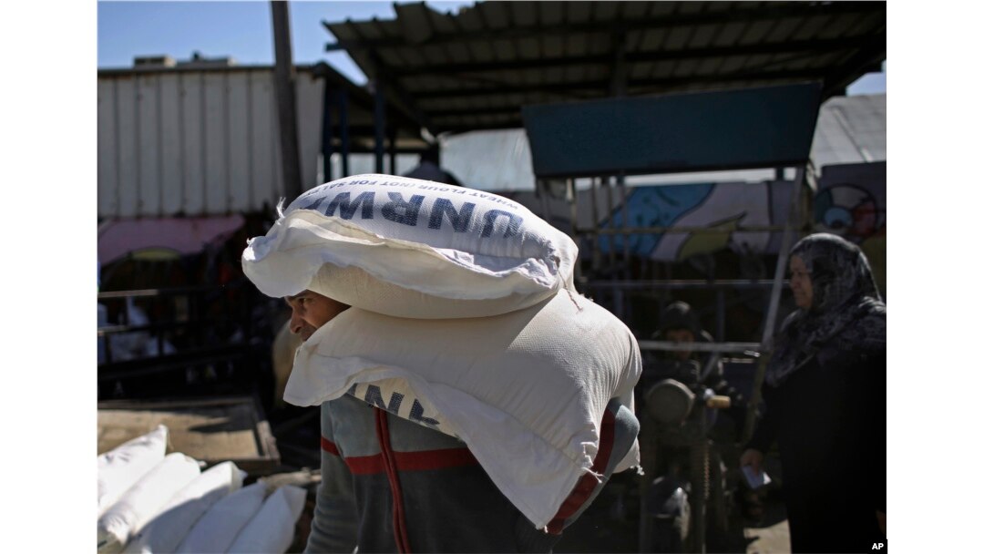 FILE - Palestinians receive food aid at a U.N. warehouse in the Shati refugee camp, Gaza City, Jan. 14, 2018.