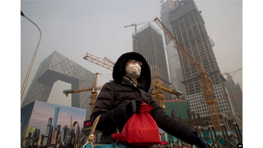 FILE - A woman wears a mask as she walks past a construction site as smog continues to choke Beijing, China, Jan. 6, 2017.