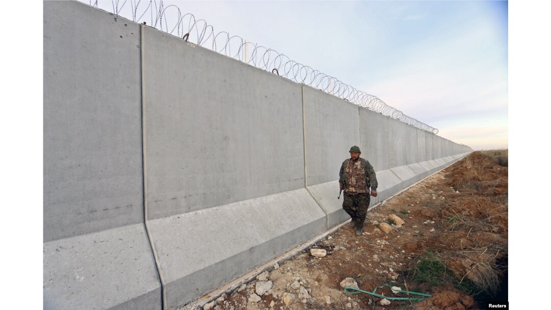 FILE - A Kurdish People's Protection Units (YPG) fighter walks near a wall, which activists said was put up by Turkish authorities, on the Syria-Turkish border in the western countryside of Ras al-Ain, Syria, Jan. 29, 2016.
