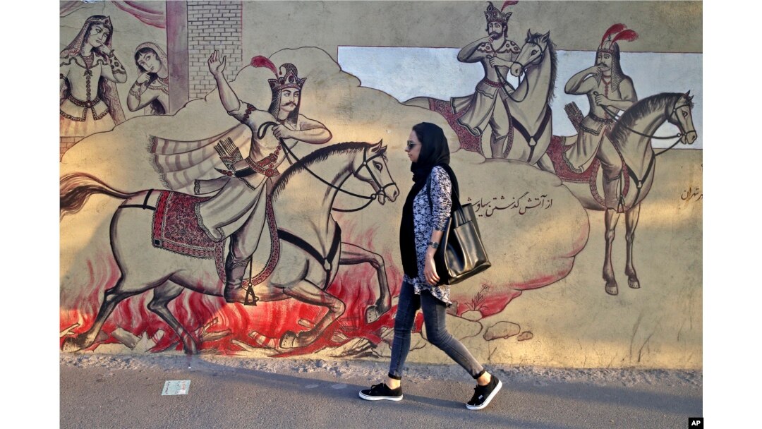 An Iranian woman walks past paintings of a Persian poetry in downtown Tehran, Iran, Monday, July 30, 2018. Iran's currency has dropped to a record low ahead of the imposition of renewed American sanctions, with many fearing prolonged economic suffering or possible civil unrest.