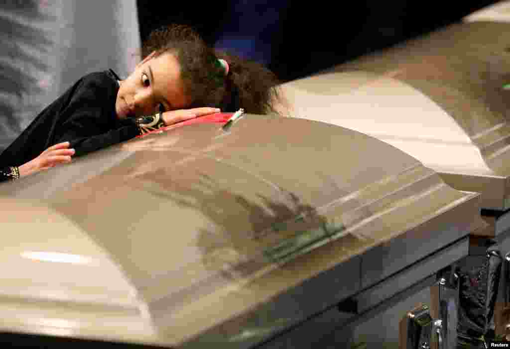 A young mourner lays her head on one of the caskets during funeral services for three of the victims of this week's deadly shooting at the Quebec Islamic Cultural Center, at the Congress Center in Quebec City, Quebec.