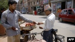 FILE - A vendor (L) exchanges money with a customer as he sells apples off his pushbike on the roadside in Lalitpur, south of Kathmandu, Nepal.