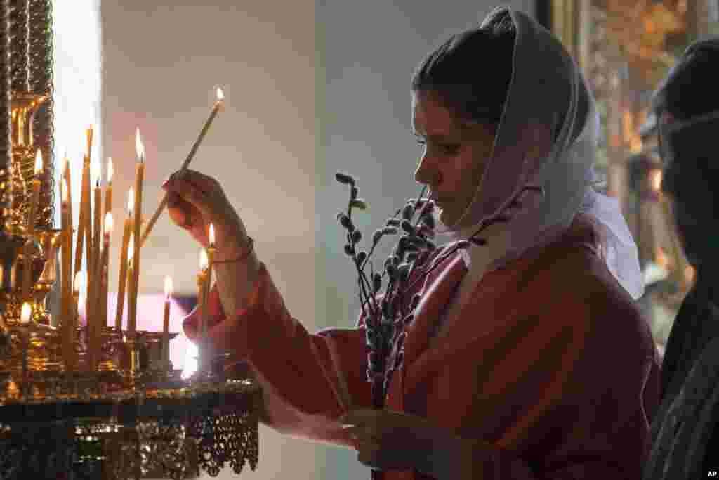 A woman lights a candle during the Palm Sunday Mass inside the St. Peter's Cathedral in the High-Petrovsky monastery in Moscow, Russia.