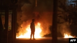 A boy stands and looks on as flames and smoke rise behind him at the scene of violence in Newtownabbey, north of Belfast, in Northern Ireland, April 3, 2021.