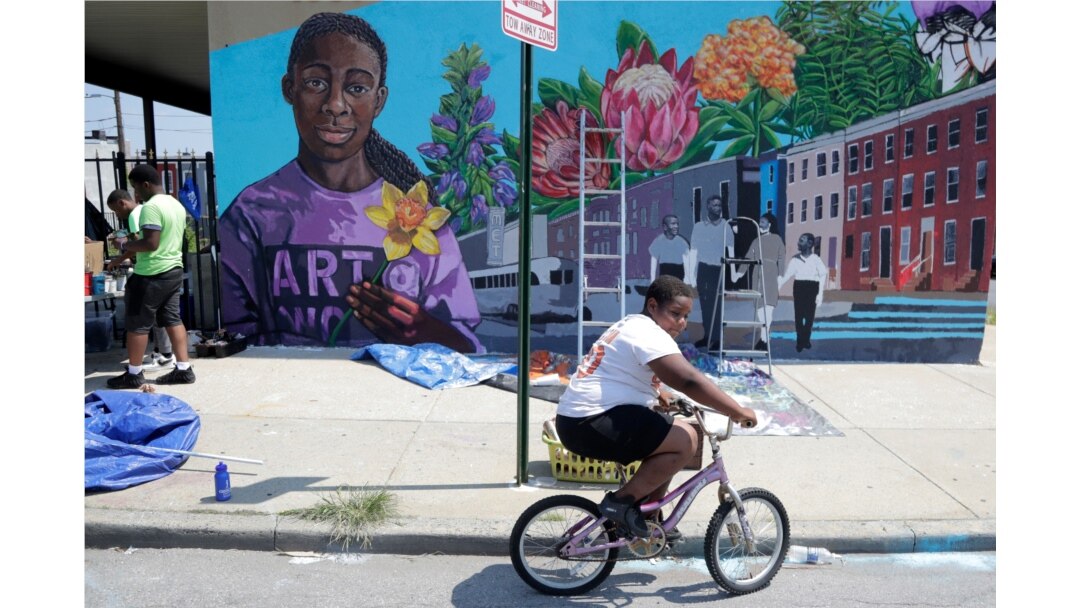 A boy rides his bicycle, July 29. 2019, after volunteering to paint a mural outside the New Song Community Church in the Sandtown section of Baltimore.