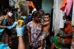 A healthcare worker checks the temperature of residents of a slum area using an electronic thermometer, in Mumbai, India, July 6, 2020.