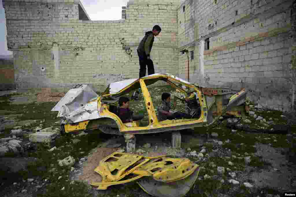 Boys play on a wrecked car in the rebel-held besieged Douma neighborhood of Damascus, Syria, April 1, 2017.