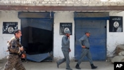 FILE - Afghan police walk past Islamic State militant flags on a wall, after an operation in the Kot district of Jalalabad province east of Kabul, Afghanistan, Aug. 1, 2016. Local officials and foreign military commanders in Afghanistan have played down concerns Islamic State is expanding activities beyond its traditional strongholds in the east.