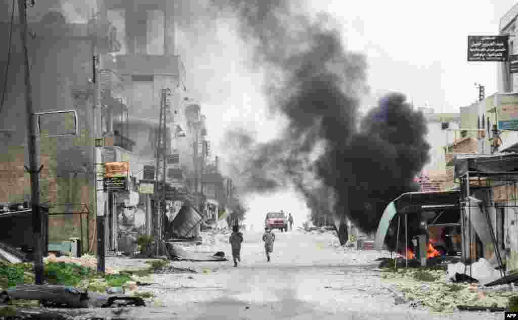 Fighters run in a street in the Syrian town of Tayyibat al-Imam in the central province of Aleppo.