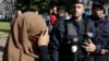 A woman wearing a full-face veil, or niqab, covers her eyes as she stands near police in Lille, France, in this September 22, 2012, file photo.
