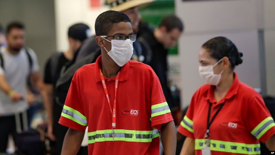 Airport employees wear masks as a precaution against the spread of the new coronavirus COVID-19 as they work at the Sao Paulo International Airport in Sao Paulo, Brazil, Feb. 26, 2020. 