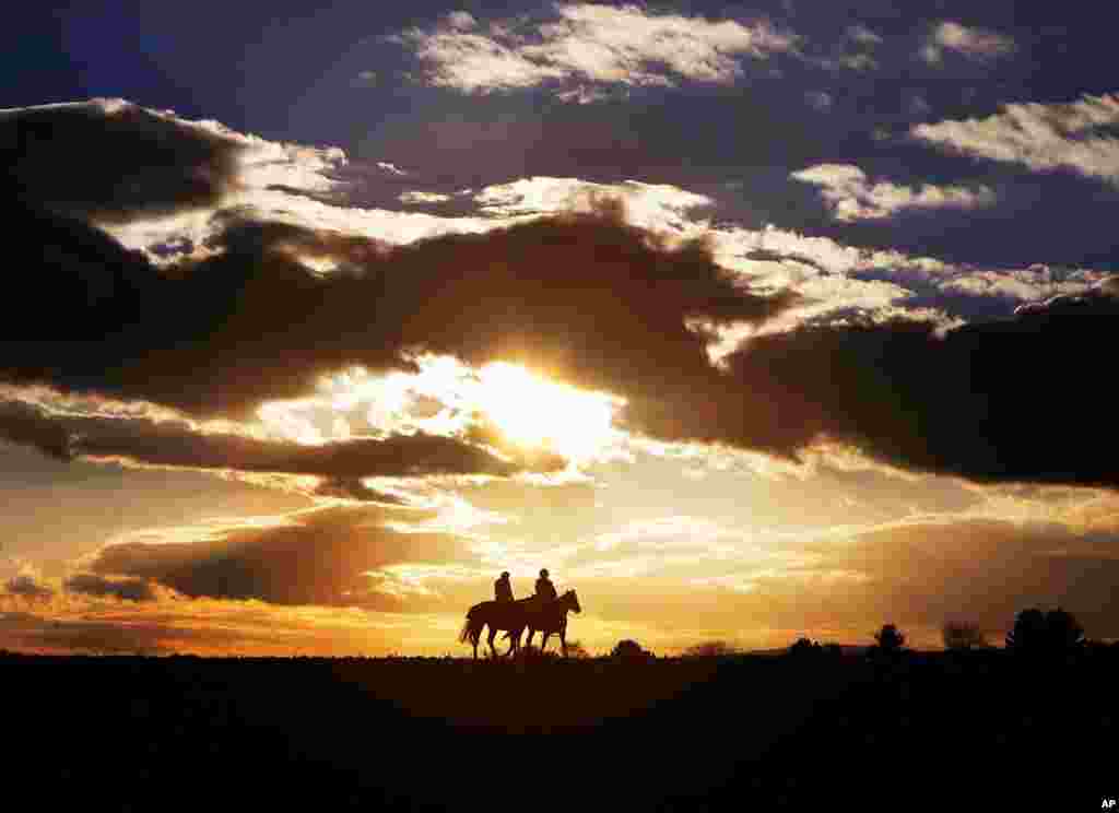 Two women ride their horses on a small road between acres of fields as the sun sets in Oberursel, Germany.