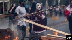 A demonstrator wearing a mask throws a plank of wood into a flaming barricade during protests in Santiago, Chile, Oct. 19, 2019.