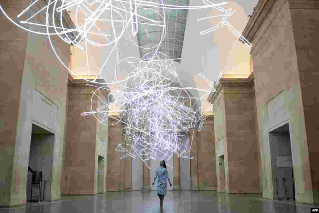 A gallery assistant poses for photographers during a photocall to promote Welsh artist's Cerith Wyn Evans new light installation entitled "Forms in Space... by Light (in Time)", made up of nearly 2km of neon lights, at Tate Britain in London.