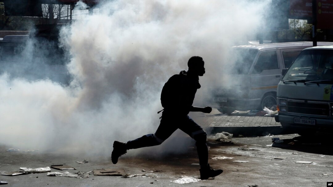 A man runs away from tear gas after making off with goods from a store in Germiston, east of Johannesburg, South Africa, Sept. 3, 2019. 