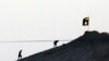FILE - In this image shot with an extreme telephoto lens and through haze from the outskirts of Suruc at the Turkey-Syria border, militants with the Islamic State group are seen after placing their group's flag on a hilltop at the eastern side of the town
