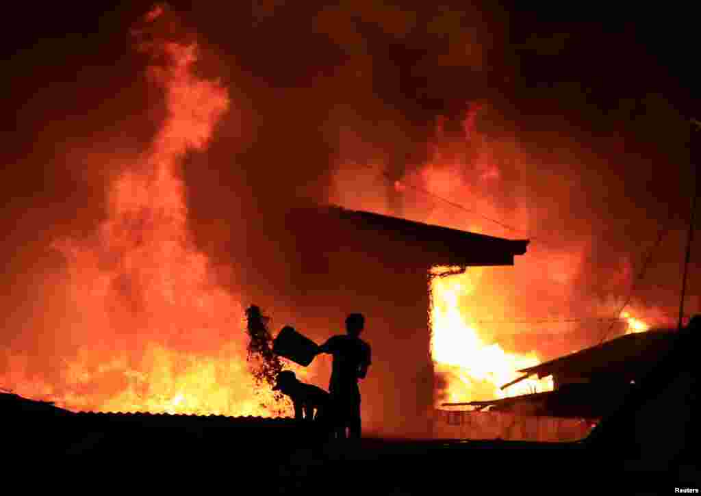 A resident throws a bucket of water at burning shanties at a community of informal settlers engulfed by a fire in Catmon, Malabon city, metro Manila, the Philippines.