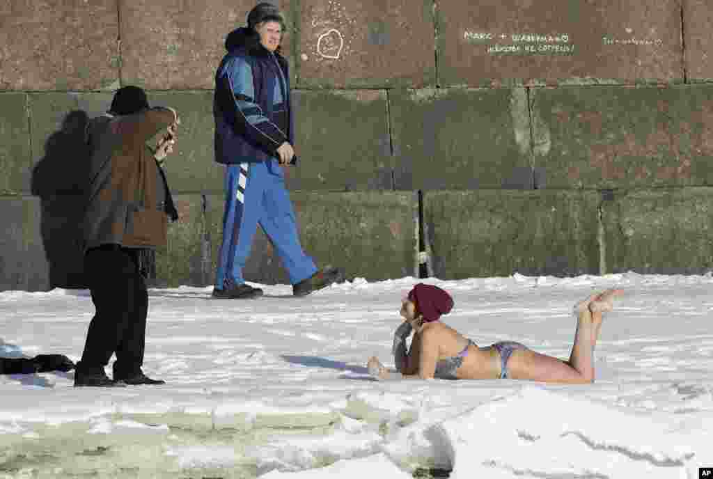 A man takes a photo of a woman who sunbathes on snow near the wall of St. Peter and Paul Fortress in St. Petersburg, Russia. The temperature in St. Petersburg is -12° C (10° F).