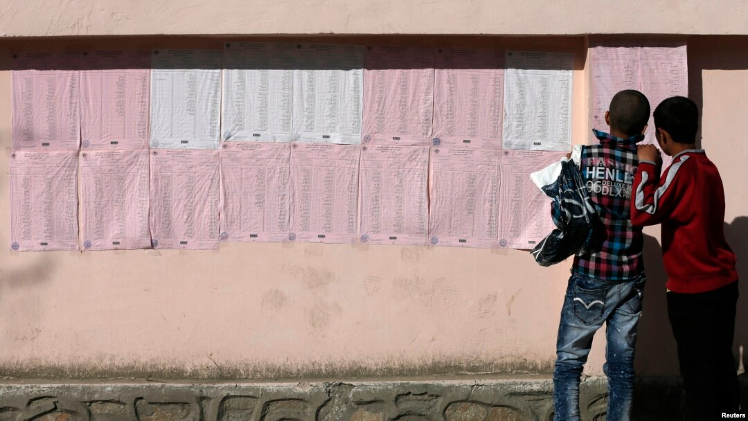 FILE - Afghan boys look on a preliminary list taped to the wall of a polling station in Kabul, April 7, 2014. 