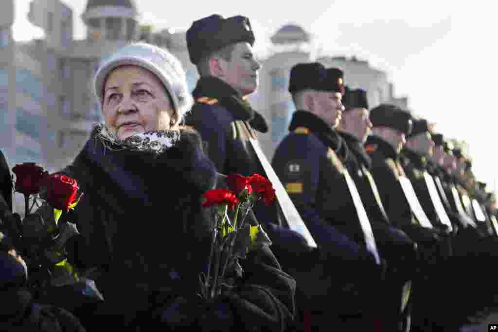 Women with flowers stand next to Belarusian military cadets holding portraits of soldiers who were killed during the Soviet war in Afghanistan, during a memorial ceremony on the Island of Tears in Minsk.