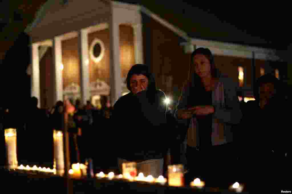 A woman covers her mouth as others look on stand near candles outside Saint Rose of Lima Roman Catholic Church near Sandy Hook Elementary School on Dec. 14, 2012.