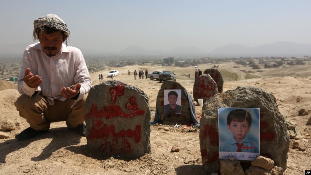 FILE - An Afghan man prays in front graves of victims of a suicide attack, in Kabul, Afghanistan, July 25, 2016. 