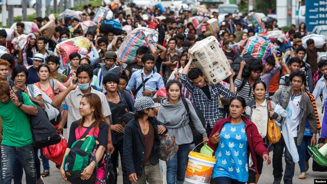 FILE - Cambodian migrant workers carry their belongings as they walk to cross the border at Aranyaprathet in Sa Kaew, June 15, 2014.