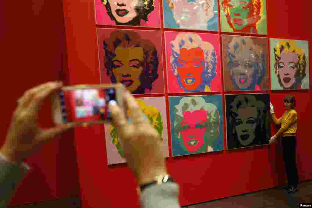 An employee poses with 10 screenprints of Marilyn Monroe by Andy Warhol as part of the exhibition, "American Dream: Pop to the Present," at the British Museum in London.