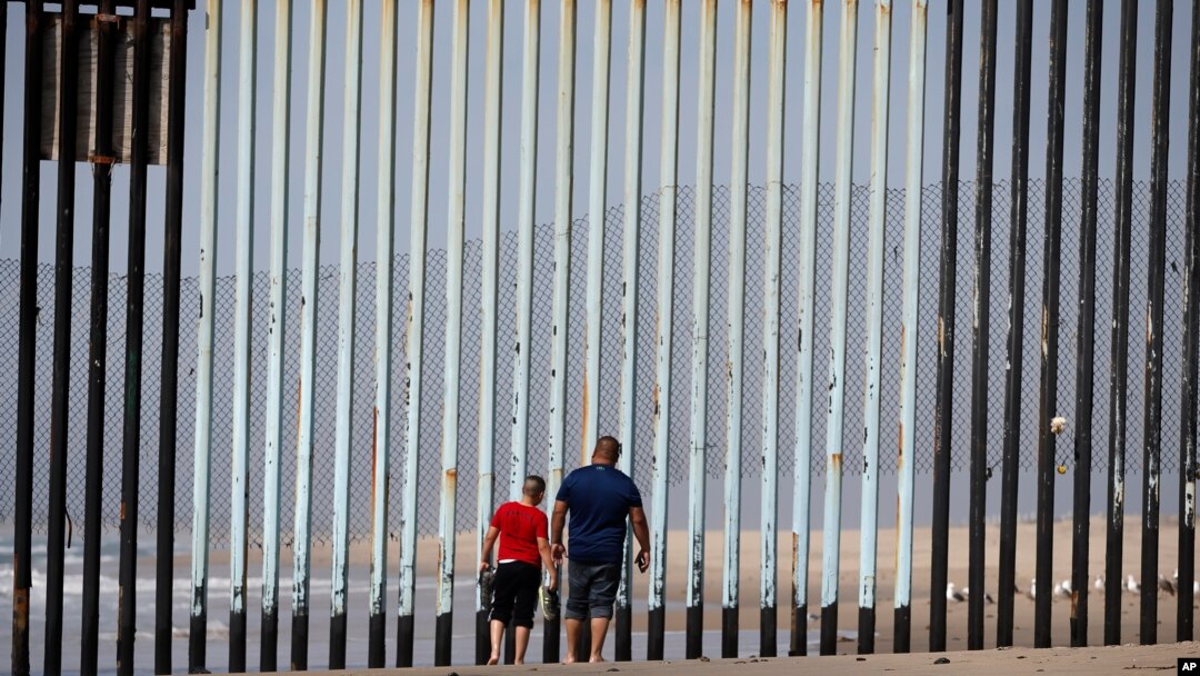 Two people walk towards metal bars marking the United States border where it meets the Pacific Ocean, March 2, 2016, in Tijuana, Mexico. Mexico's President Enrique Pena Nieto has said his country does not intend to pay.