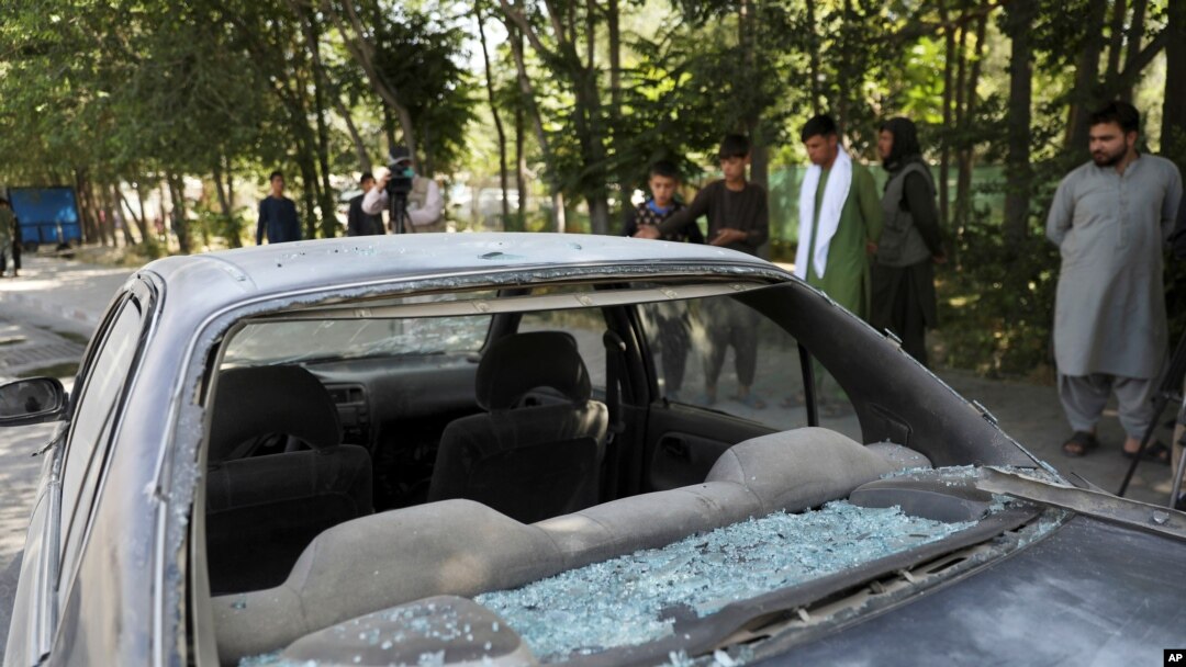 Afghan men look at a damaged car after a roadside bomb explosion in Kabul, Afghanistan, June 6, 2021.